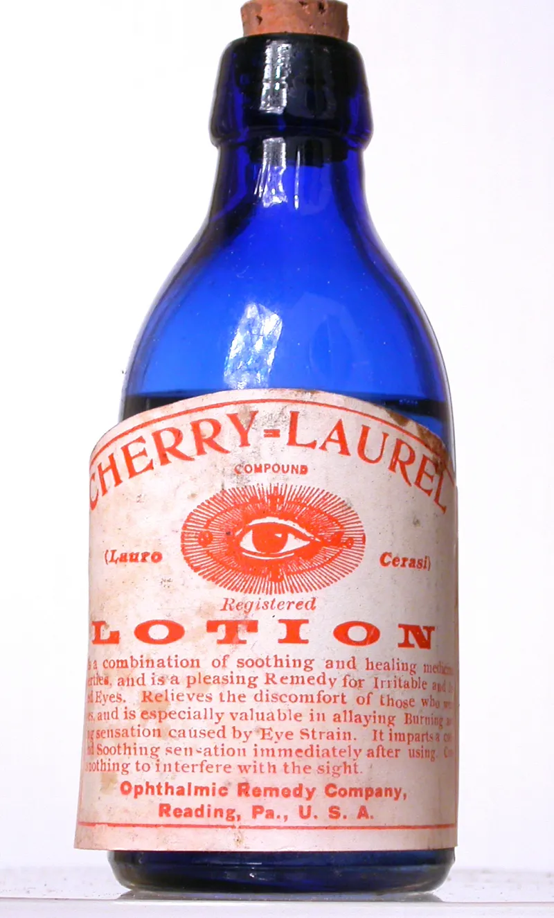 An image of an old blue glass bottle with a cork and label that describes 'Cherry Laurel Lotion'.