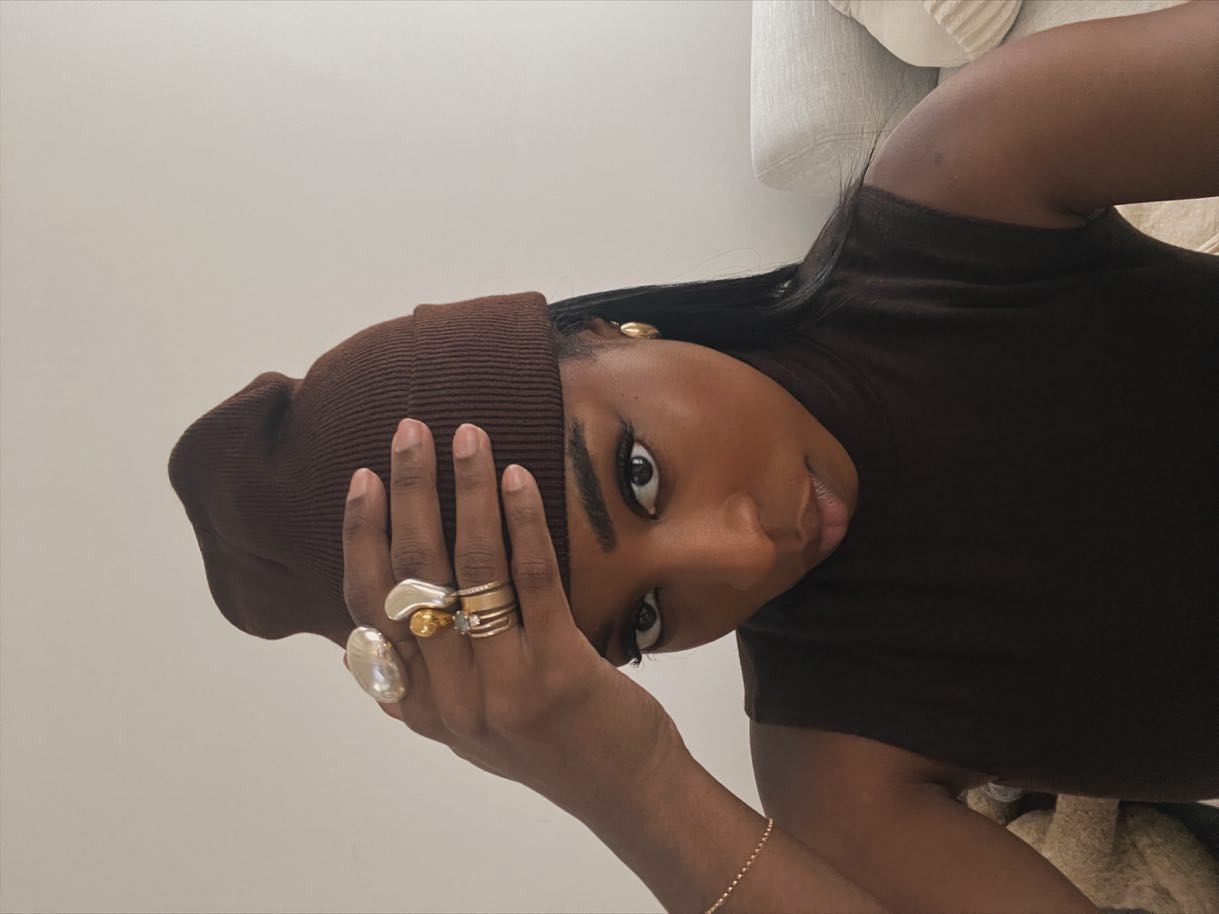 Cortne wears a brown hat, mixed metal rings, and a black tank top.